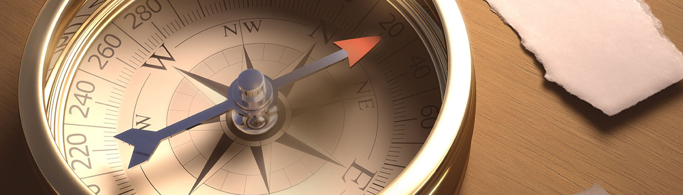 A stylized compass laying on a wood table.