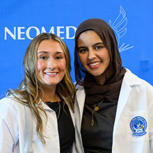 Two pharmacy students pose in their white coats.