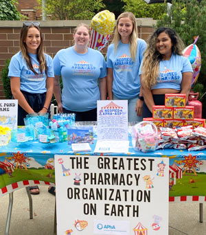 Students at a fair at a table with a sign that says The Greatest Pharmacy Organization on Earth.