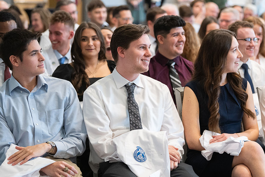 A group of students chat while seated at a white coat ceremony.