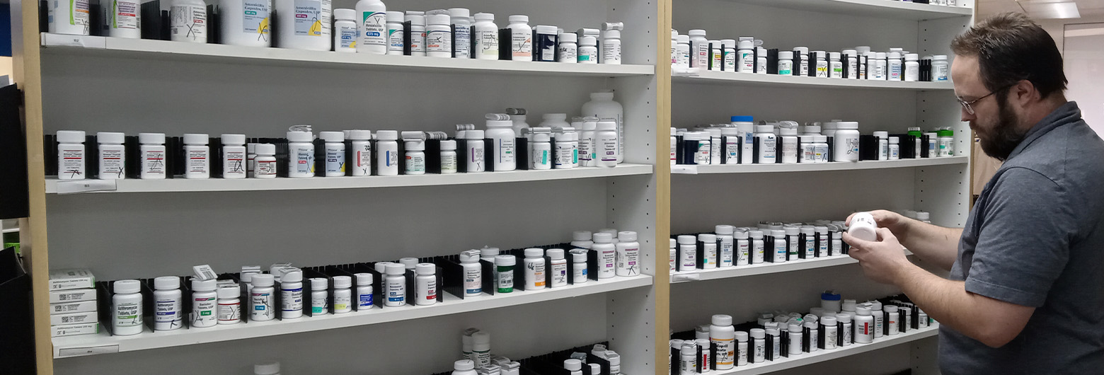 A pharmacist checks over the counter supplies on a row of shelves