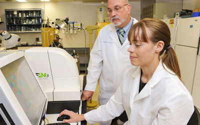 A man and a woman in white coats at work in a NEOMED lab.
