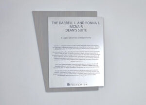 A metal plaque on a wooden background commemorates The Darrell L. and Ronna J. McNair Dean’s Suite