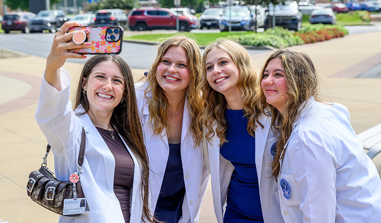 Four new dentistry students stand for a selfie in their white coats.