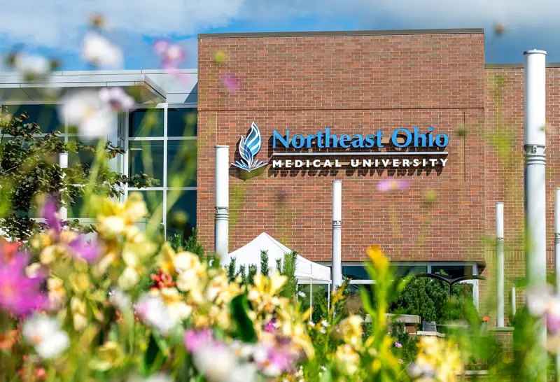 The NEOMED logo appears on the main building with flowers in the foreground.
