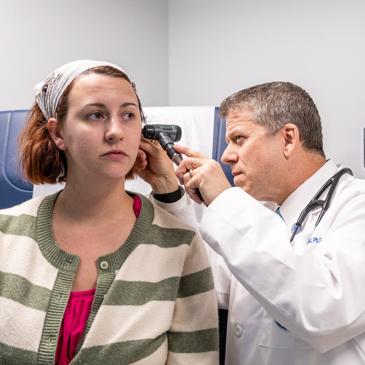 A physician uses an otoscope to examine a seated patient’s ear in a clinical exam room.