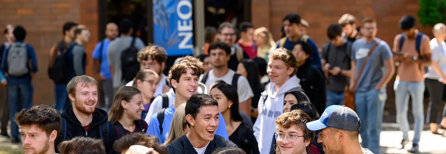 A large group of students gathers and talks in a sunny NEOMED courtyard.