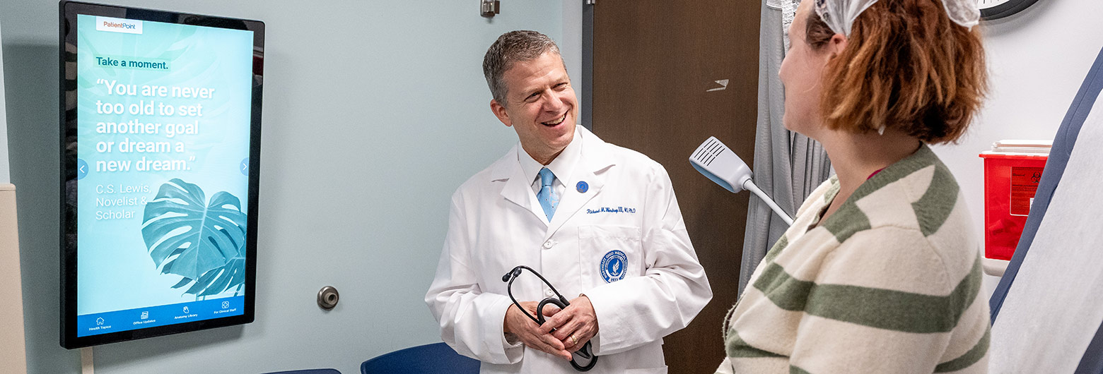A physician in a white coat greets a patient at the beginning of an appointment.