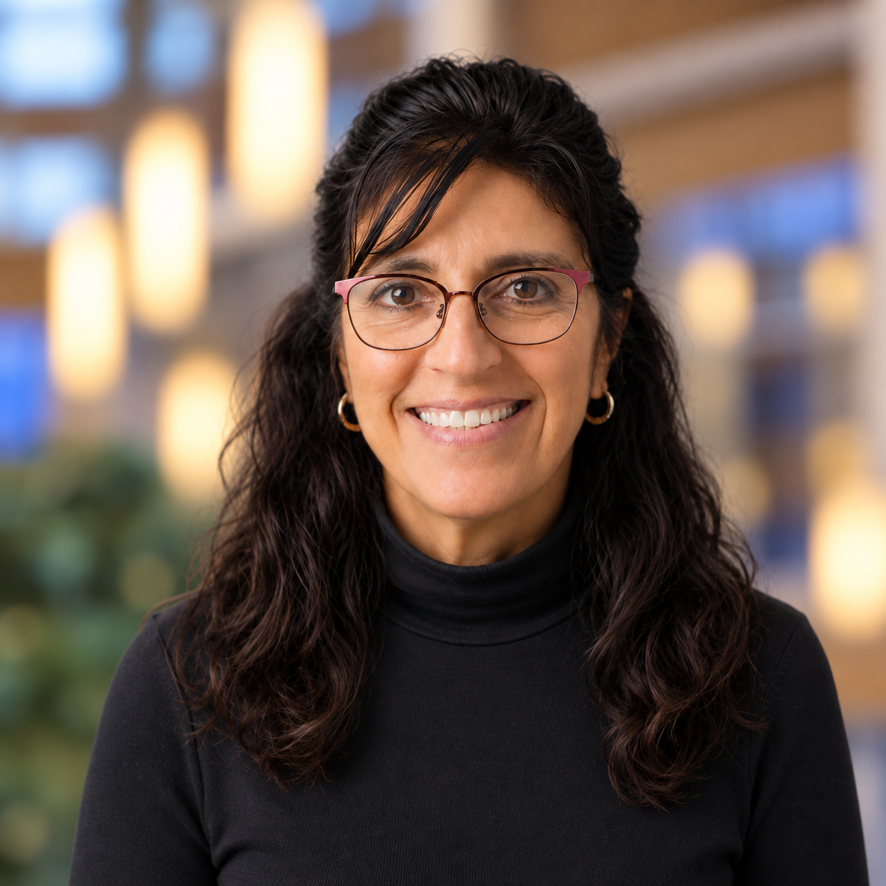 Professional headshot of a smiling woman with dark hair and glasses.