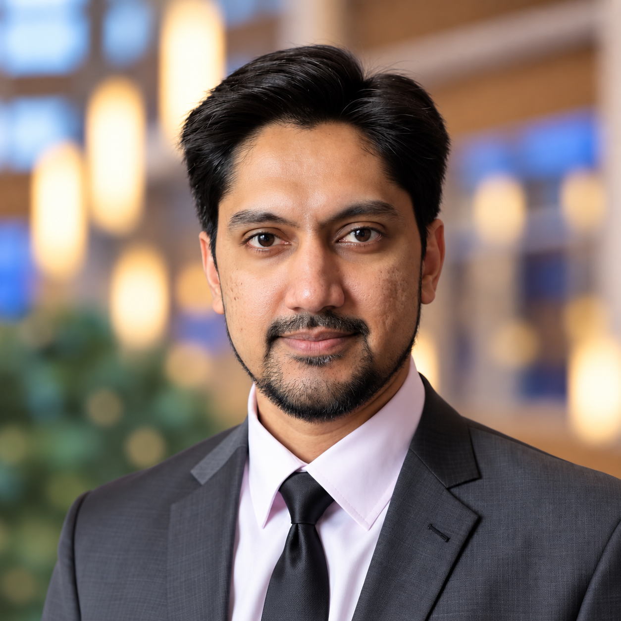 Professional headshot of a man with dark hair and a beard wearing a suit and tie.