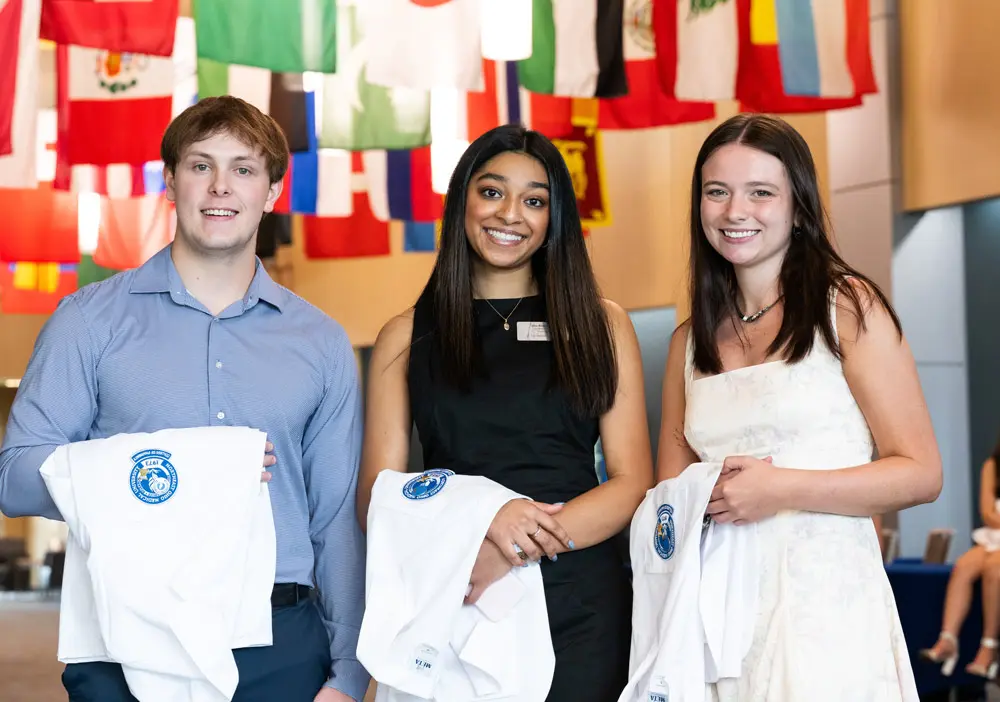 Three pharmacy students hold their white coats.