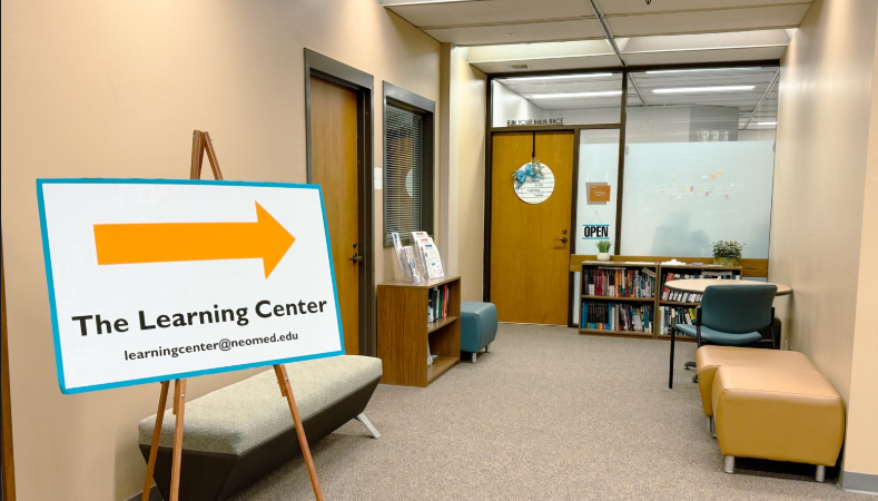Interior hallway leading to the NEOMED Learning Center, with seating, bookshelves, and a large directional sign pointing toward the Learning Center entrance.