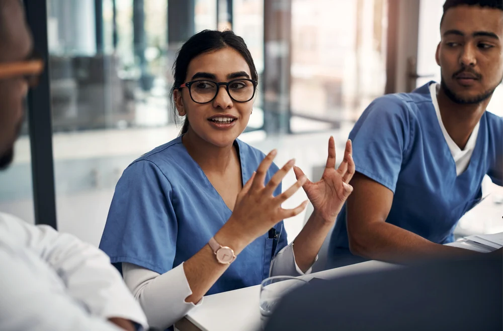 A pharmacist gestures while making a point during a team meeting in a hospital.