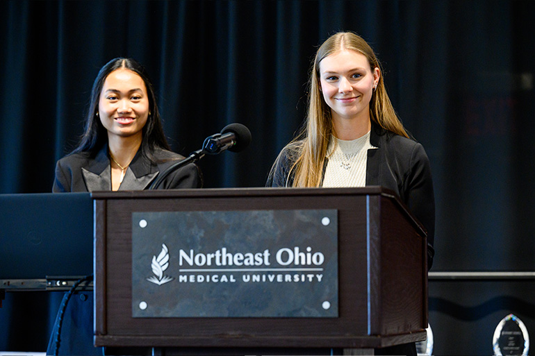 Two young woman in business attire stand behind a podium