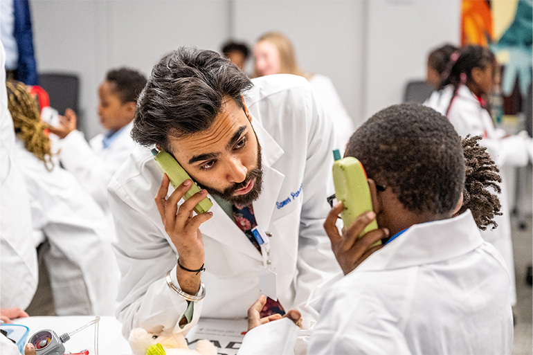 A man in a white coat talks on a toy phone with a child in a white coat