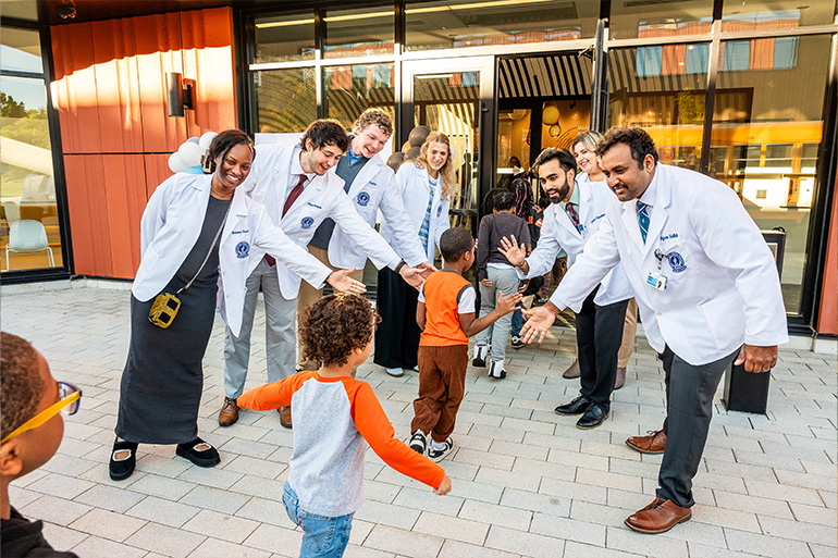Several people in white coats line up to make a welcome corridor to high five children as they walk by