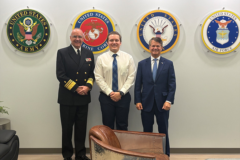 Three men stand in front of round emblems of the U.S. Armed Forces