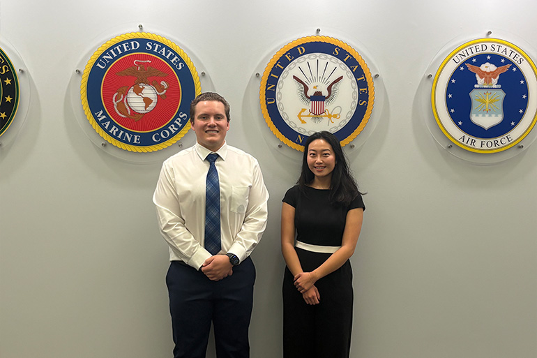 a man and a woman pose in front of round emblems of the U.S. Armed Forces