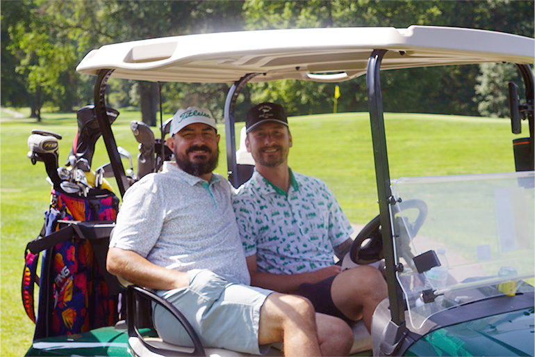 Two men ride in a golf cart.
