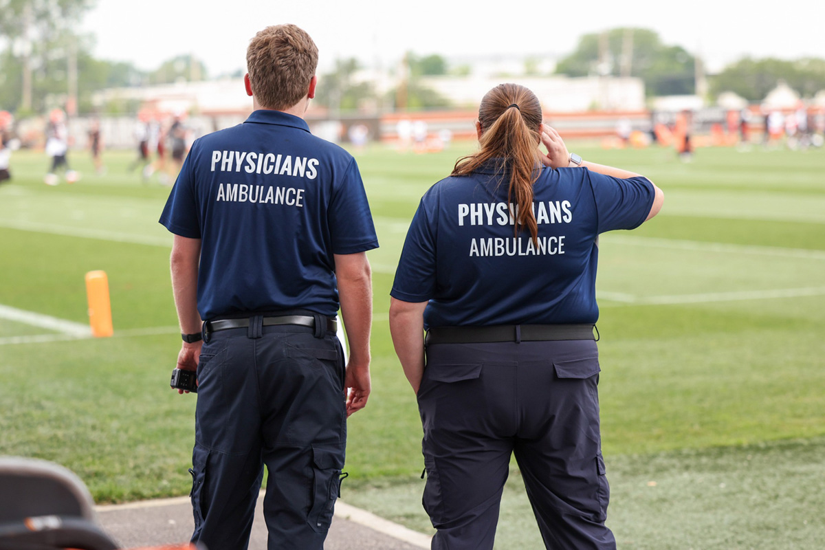 man and woman with physician's ambulance shirts looking ahead into field at stadium