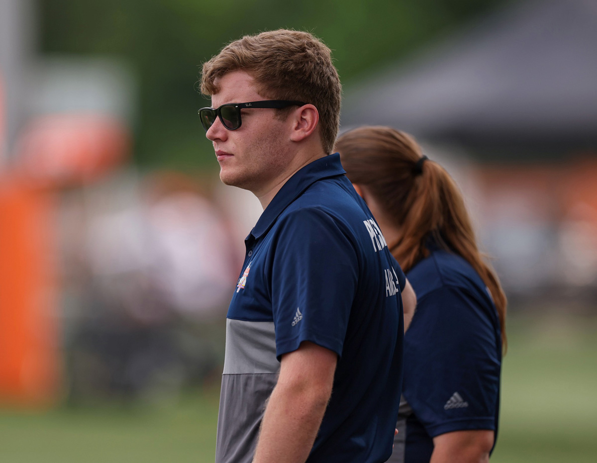 man wearing glasses looking to the left side with a woman standing next to him with a blurry background at a stadium