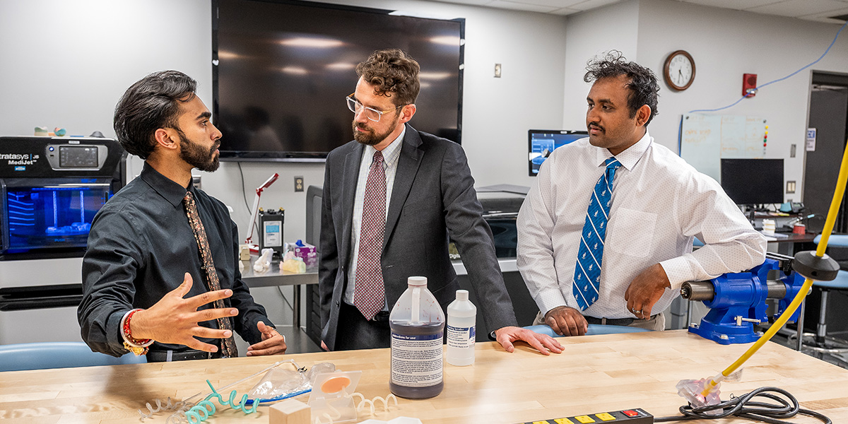 Man explains something at a workbench to another man, while another looks on
