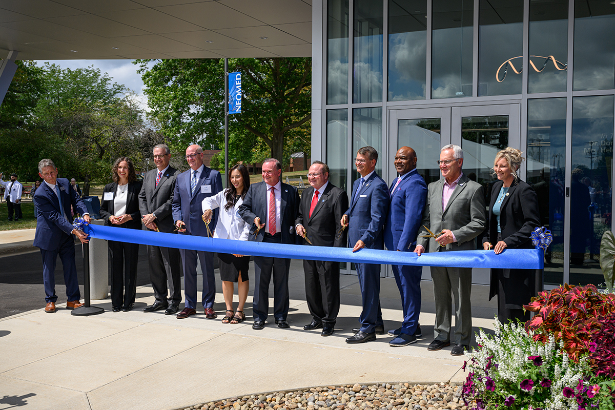 Large group of people line up behind a blue ribbon, with scissors for the Bitonte College of Dentistry ribbon-cutting ceremony