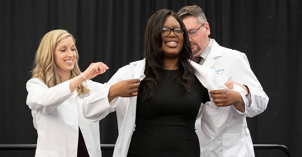 A first-year master of medical science in anesthesia student smiles as she dons her white coat for the first time.