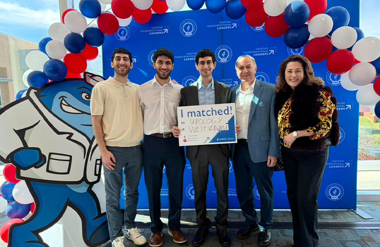 Young man in a suit holds a Match Day sign, surrounded by his family