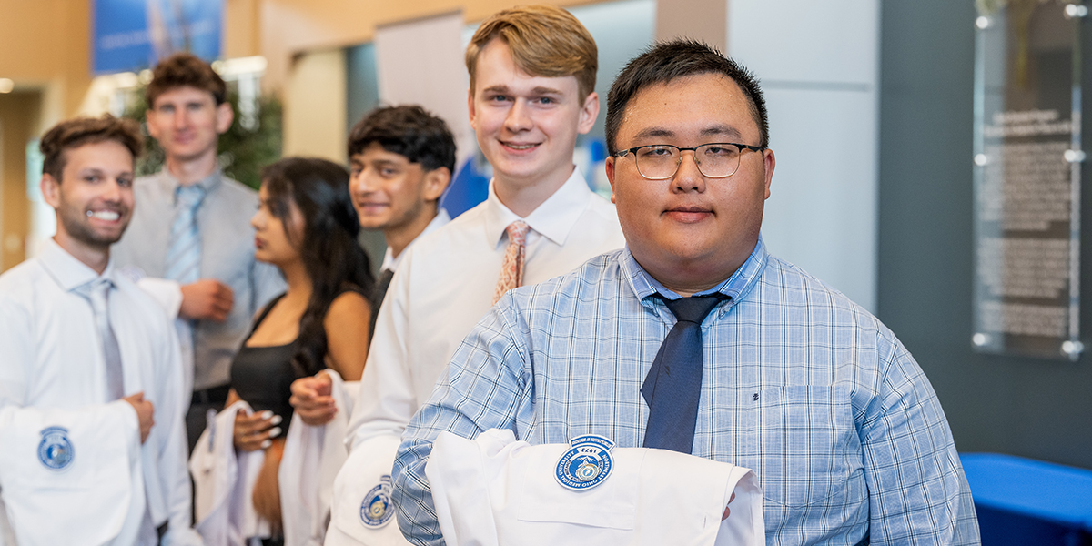 Young man in blue shirt leads a line of new dentistry students waiting for their White Coat Ceremony
