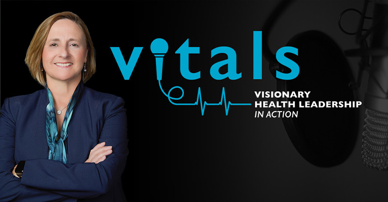 Woman in suit stands with arms folded in front of black background and VITALS logo