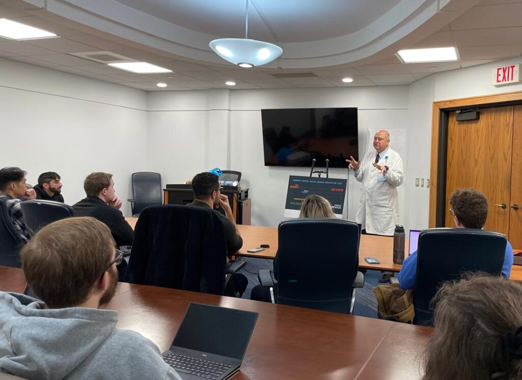 A physician stands before a seated group in a modern room.