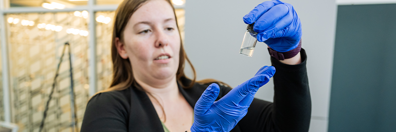 woman wearing blue gloves holds a test tube full of a gel