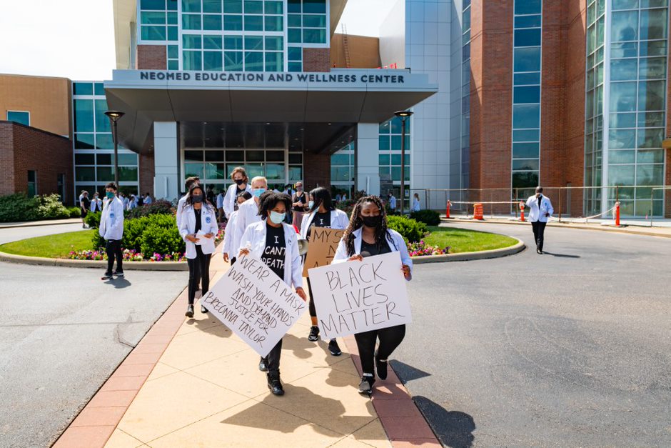 Students carrying signs walking out to the road in front of NEOMED