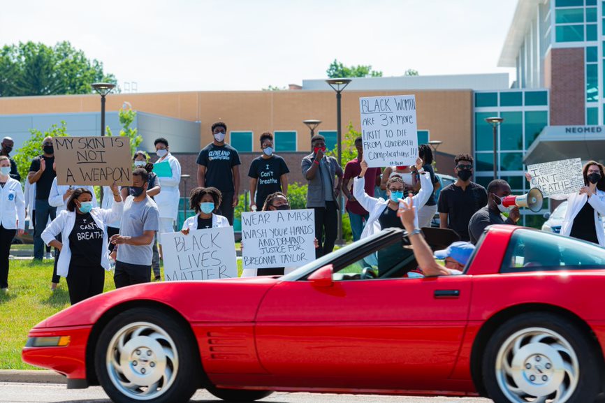 A community members drives their car past the White Coats for Black Lives protest