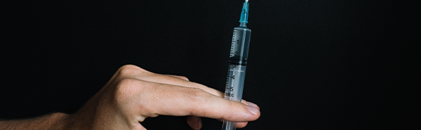 Hand holding vaccine upright in front of black background
