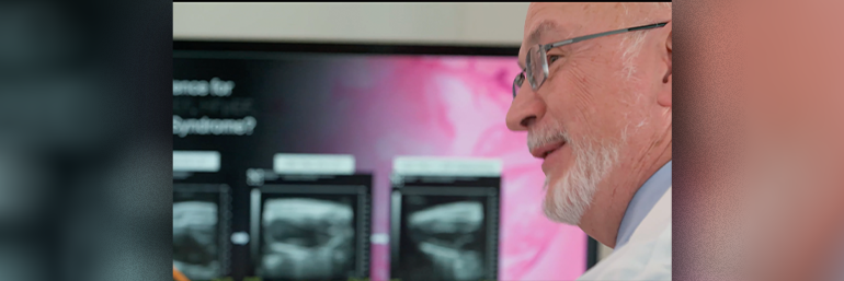 Older man with glasses and white beard in front of a pink screen examine slide Images
