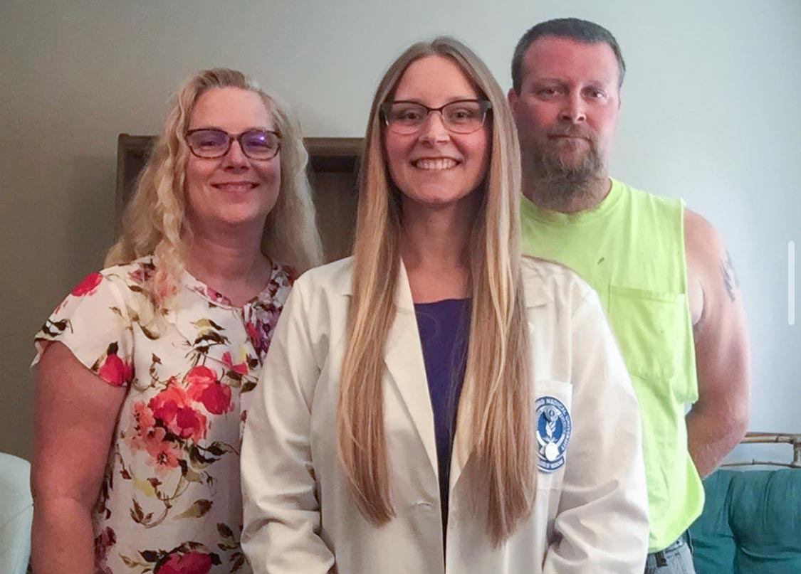 A medicine student in a white coat stands with her parents.