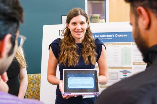 A woman holding an iPad makes a presentation about her innovation before judges.