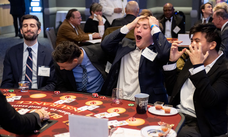 A group of men at a casino table react to a card turn.