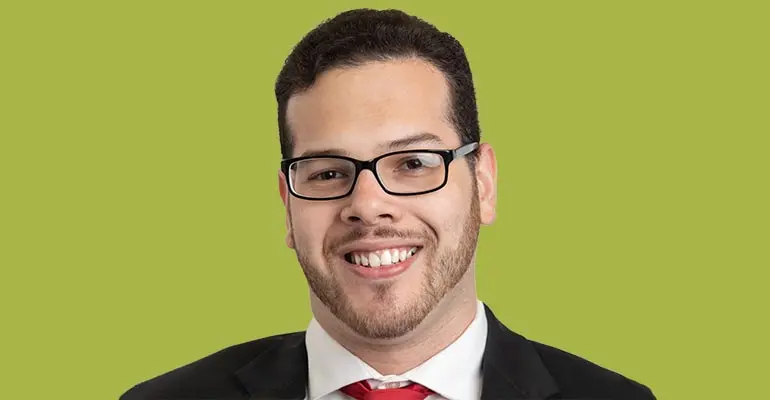 A smiling man in a coat and tie with a green background.