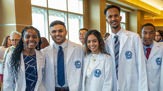 Five medical students in white coats following a ceremony at NEOMED.
