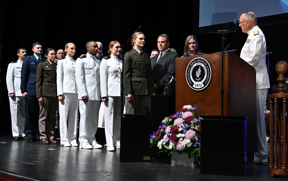 Uniformed graduates stand in line on stage during a Northeast Ohio Medical University military commissioning ceremony.
