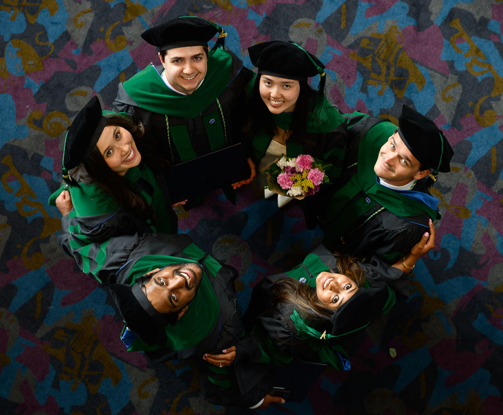 Six graduates in academic regalia stand together and look up toward the camera after commencement.