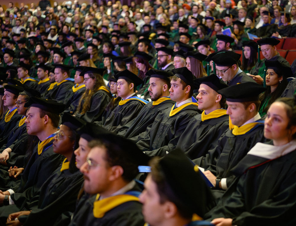 Graduates in caps and gowns sit in rows among faculty and guests during a commencement ceremony.