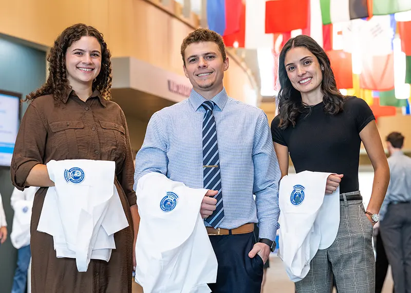 Three dental students hold their white coats after just receiving them at a ceremony.