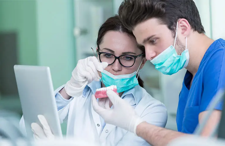 Two dental professionals examine a denture.