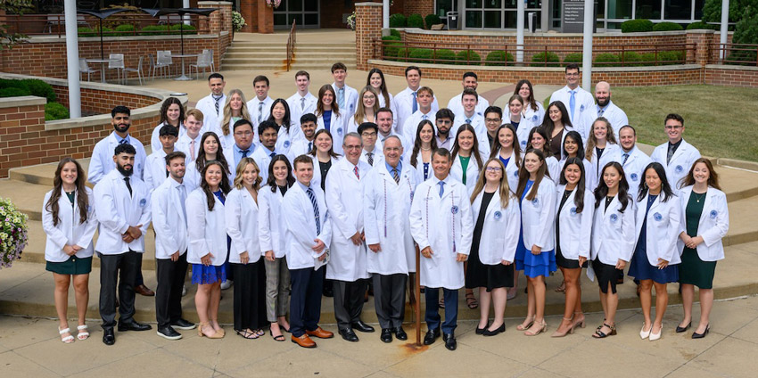 Standing in white coats, the first class in the Bitonte College of Dentistry stands outside of NEOMED's main entrance.