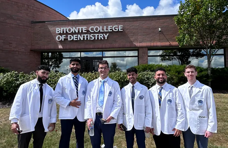 Six new dental students stand wearing their white coats, which they just received at a ceremony.