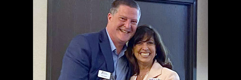 A man congratulating a woman, who is holding a plaque.
